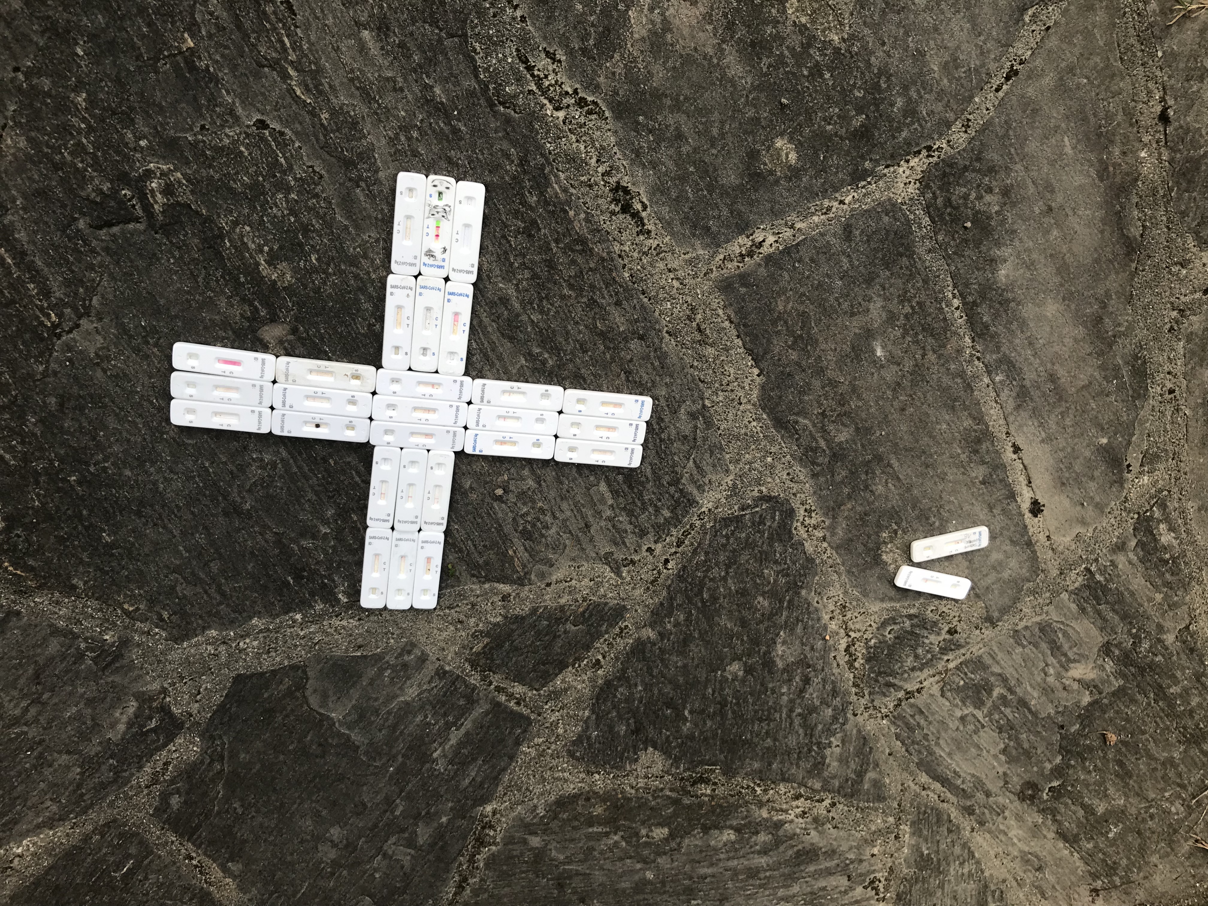 Weiße Testkits aus Plastik in Kreuzform auf Steinboden.