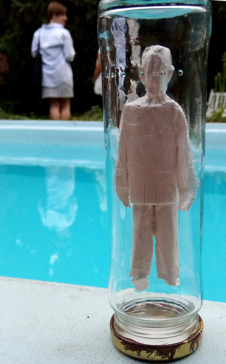 Acht Glaszylinder, darin menschliche Figuren aus Karton und Klebeband, weiß bemalt. Höhe: 15 cm, Durchmesser: 4,5 cm