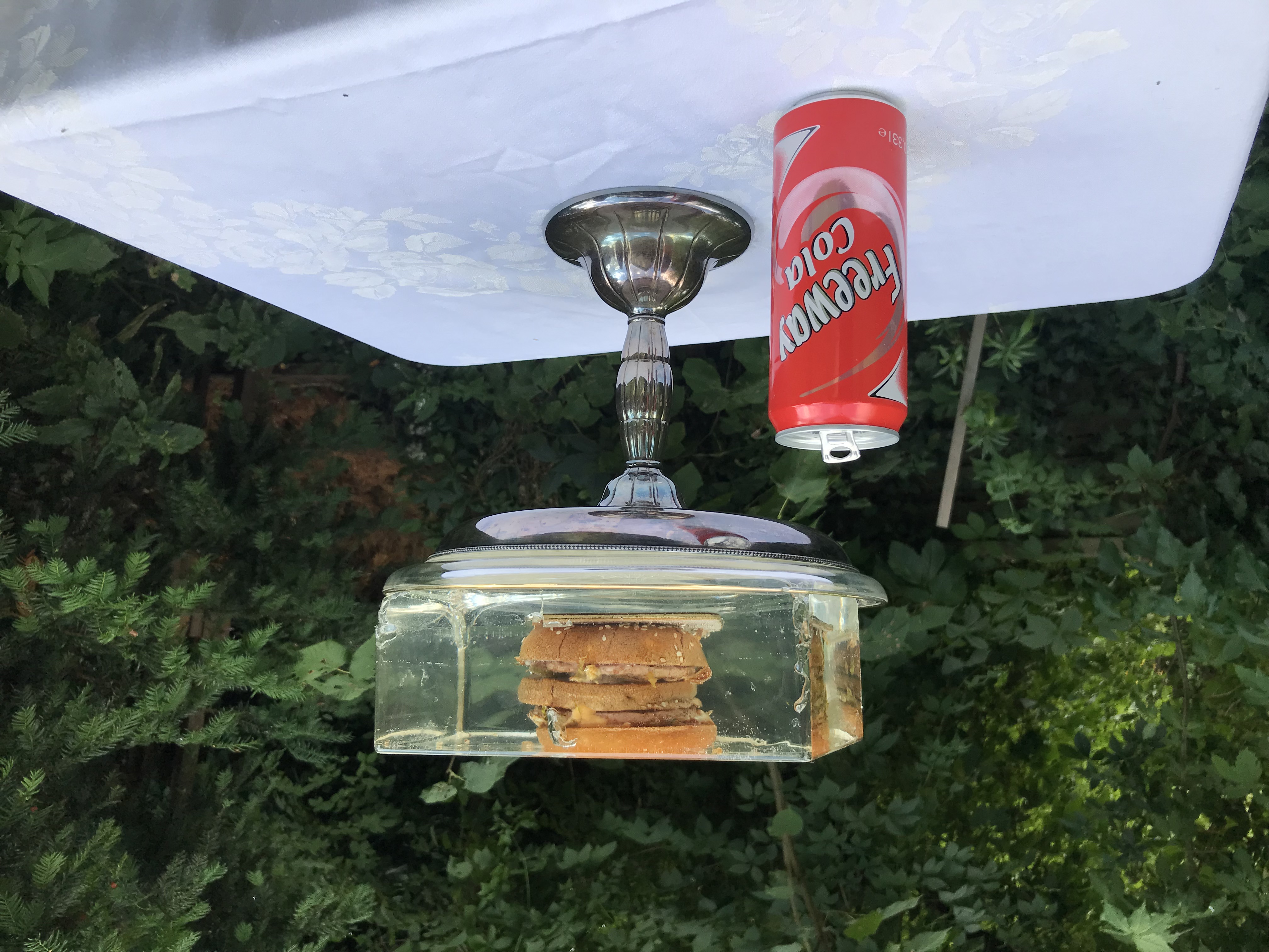 Big Mac in Epoxyharzblock eingegossen auf einem silbernen Kelch. Daneben steht eine rote Dose Freeway-Cola.