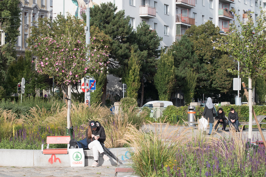 Menschen sitzen in einer Garten-/Parkanlage in der Sonne.