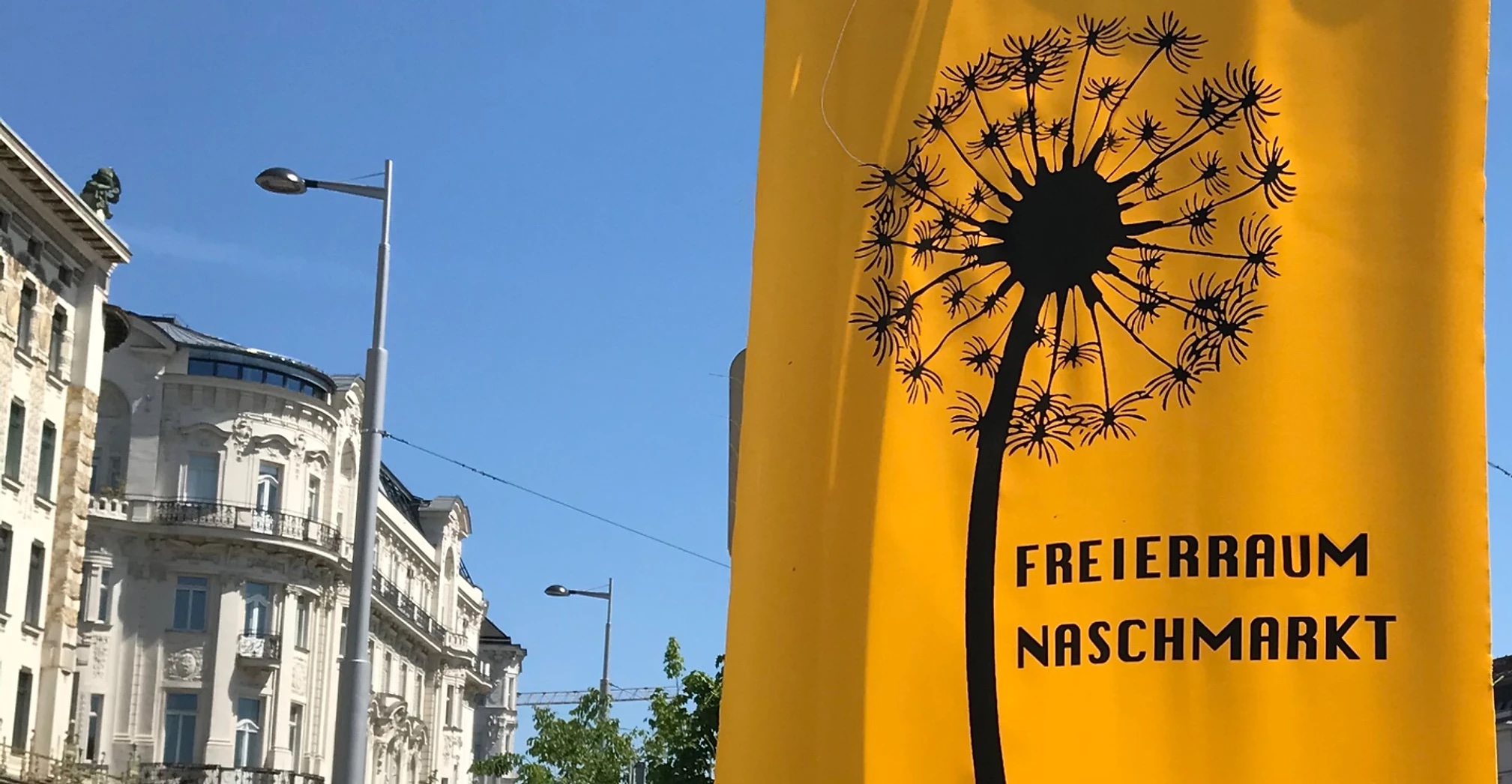 Farbfoto, Ausschnitt: Gründerzeithäuser und eine gelbe Fahne mit schwarzer Pusteblume und der Aufschrift FREIRAUM NASCHMARKT.