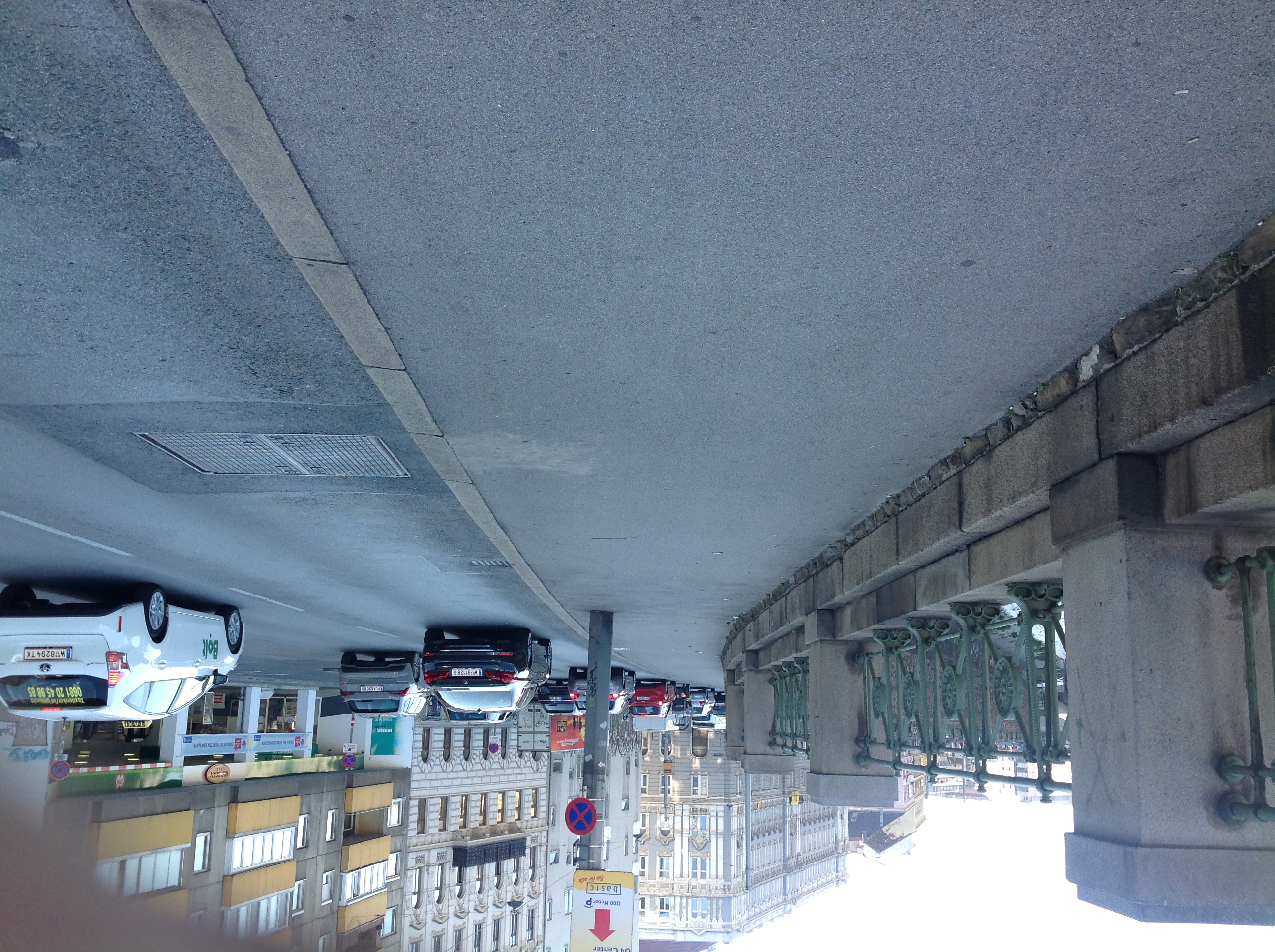 Farbfoto: Geländer, Gehweg, Fahrbahn, Häuserzeile (von links nach rechts)