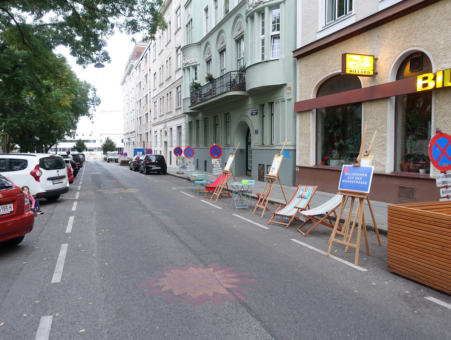 Als Wohn­straße verordneter Straßenzug, allerdings mit herkömmlichem Straßenquerschnitt inkl. Schrägparkern. Am Asphalt der Fahrbahn sind ein paar Blumen aufgemalt. Daneben stehen temporär Sessel und Wohn­straße-Schautafeln von der Initiative Space and Place.